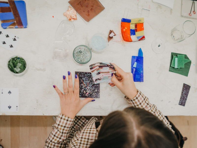 An overhead shot of a glass fusing art class with a woman working on some glass coasters
